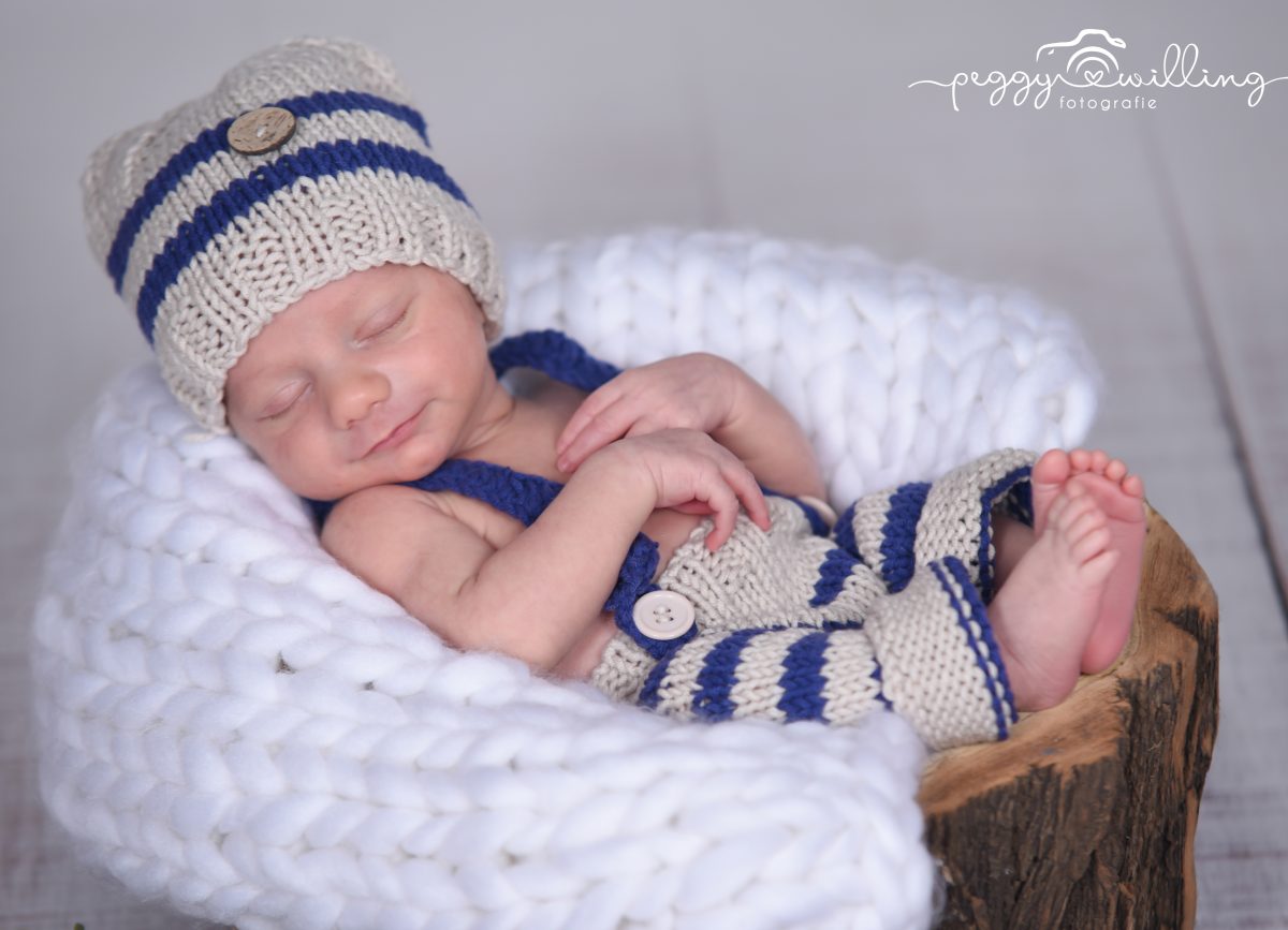 Baby liegend auf Holzstamm mit Decke und Mütze